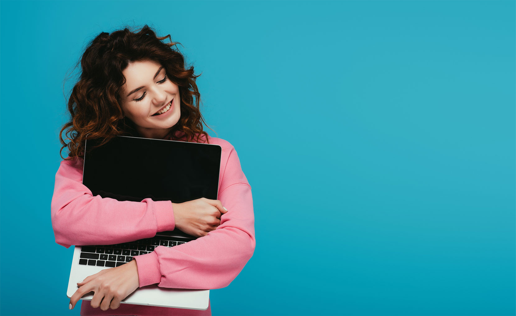Woman in pink jumper hugging a laptop computer on a blue background.